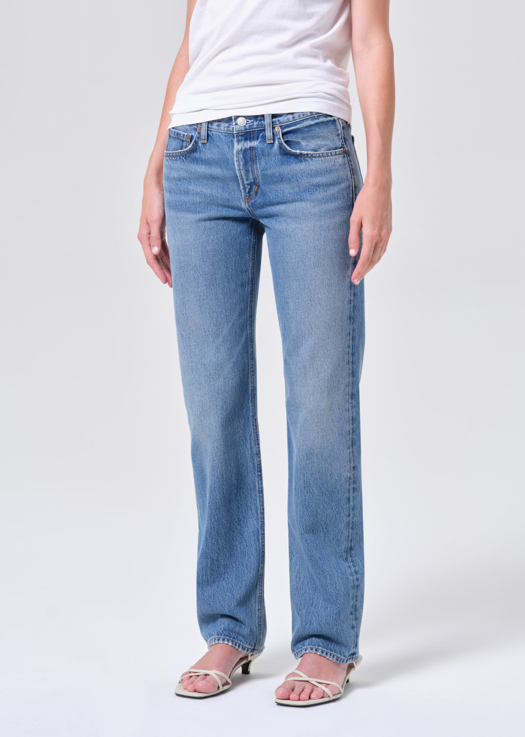 Person wearing light blue jeans and a white top on a plain background