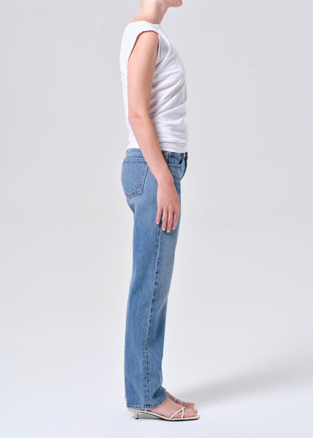 Person wearing light blue jeans and a white sleeveless top on a plain background