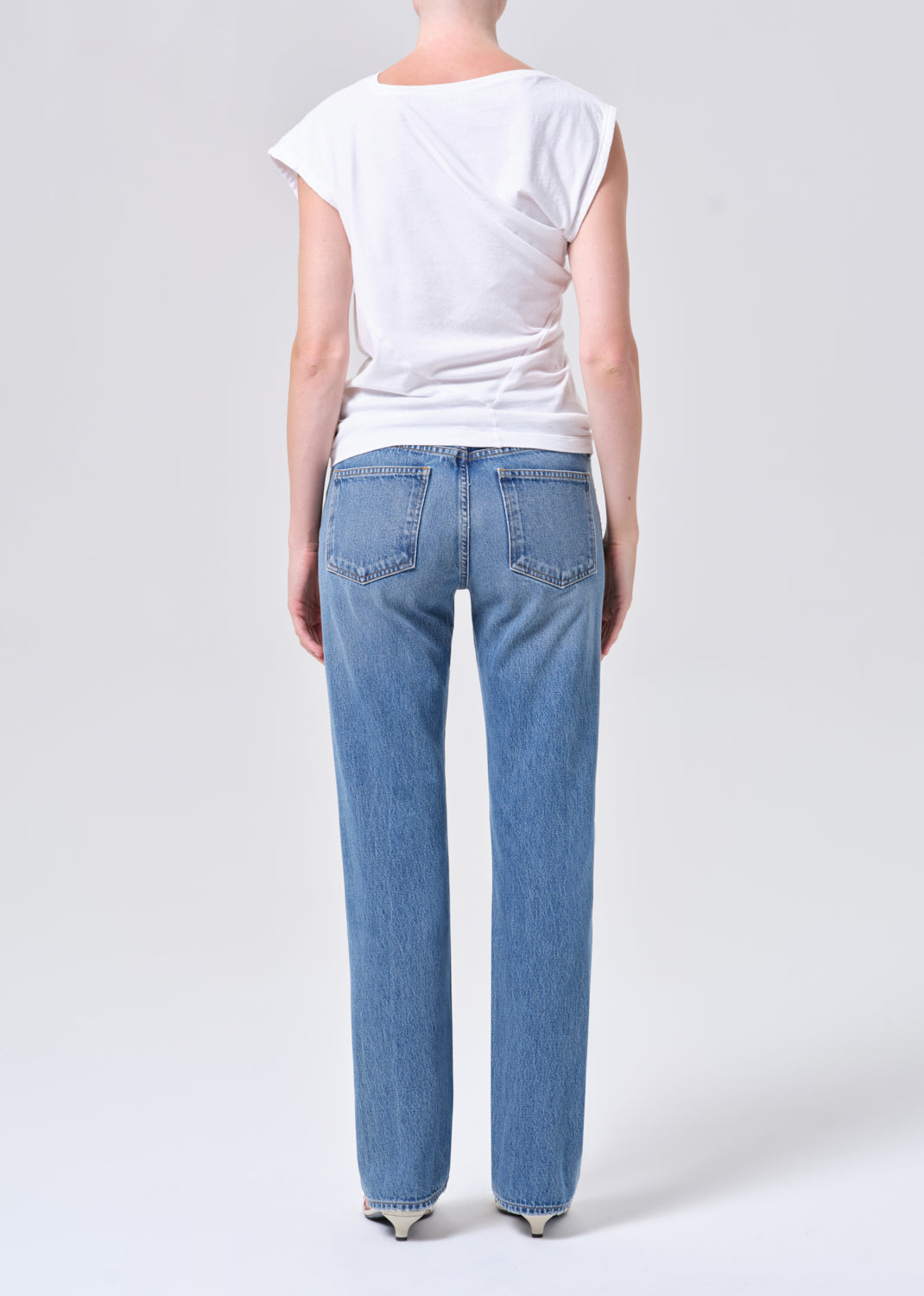 Person wearing blue jeans and a white t-shirt on a plain background