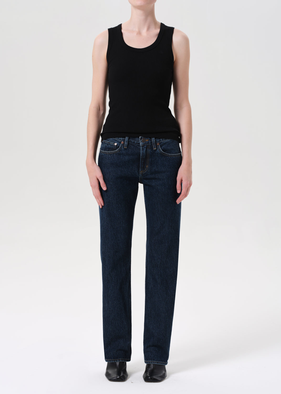 Person wearing a black sleeveless top and dark blue jeans on a white background