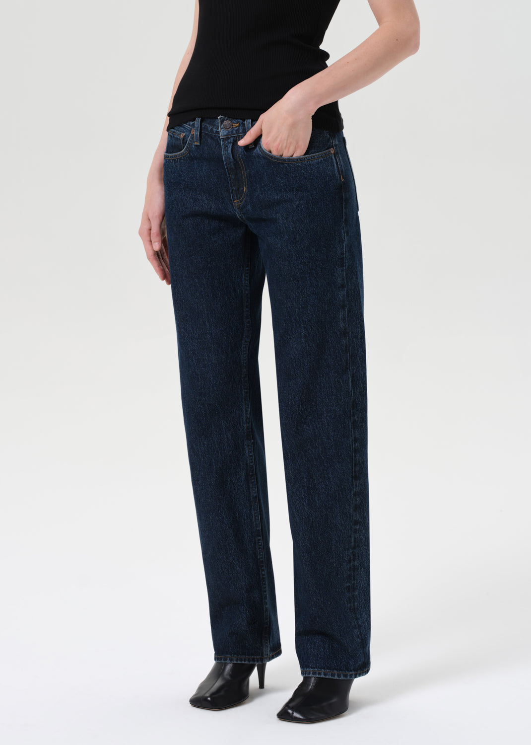 Person wearing dark blue jeans and black shoes on a white background