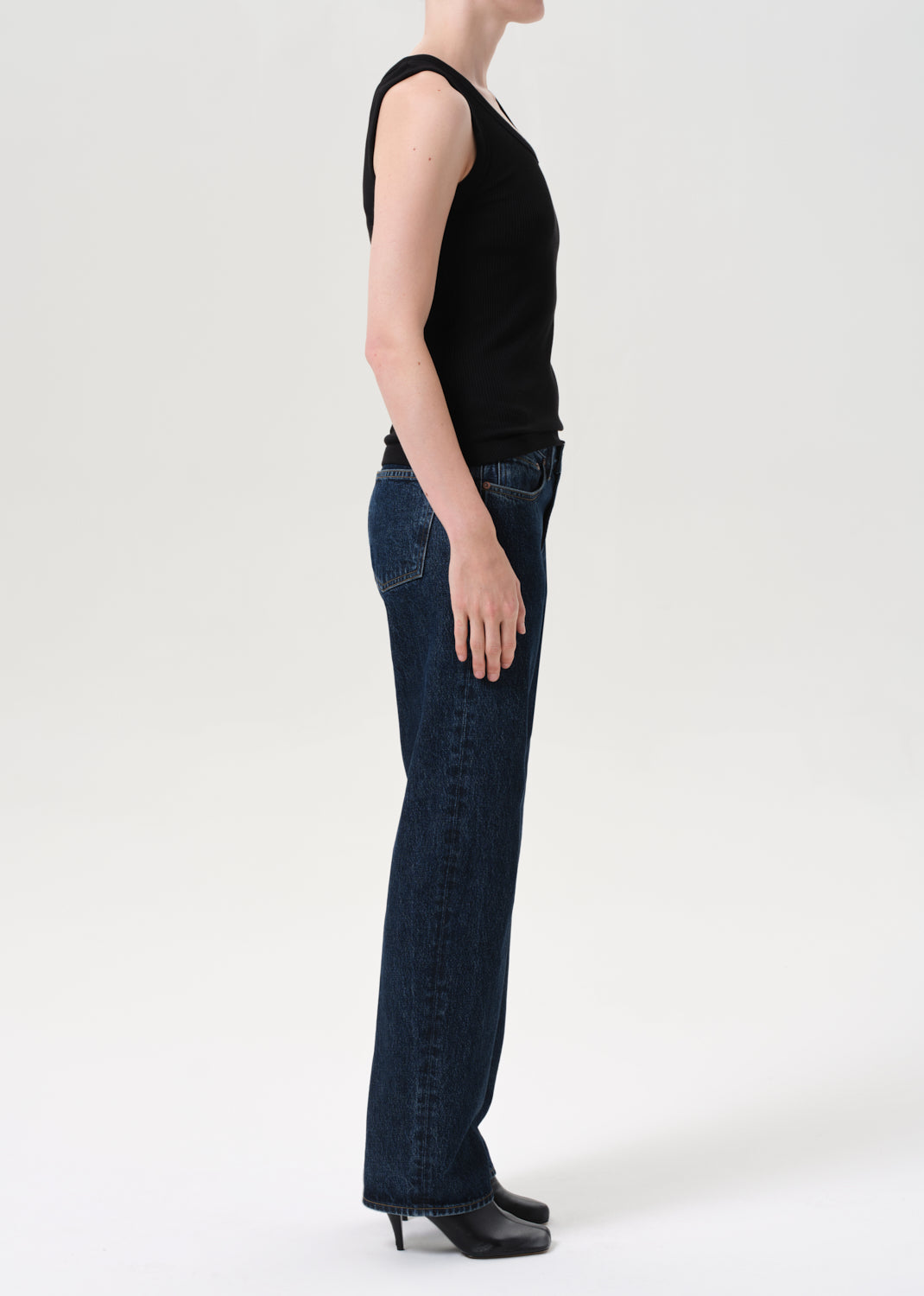 Person wearing a black sleeveless top and dark blue jeans on a white background