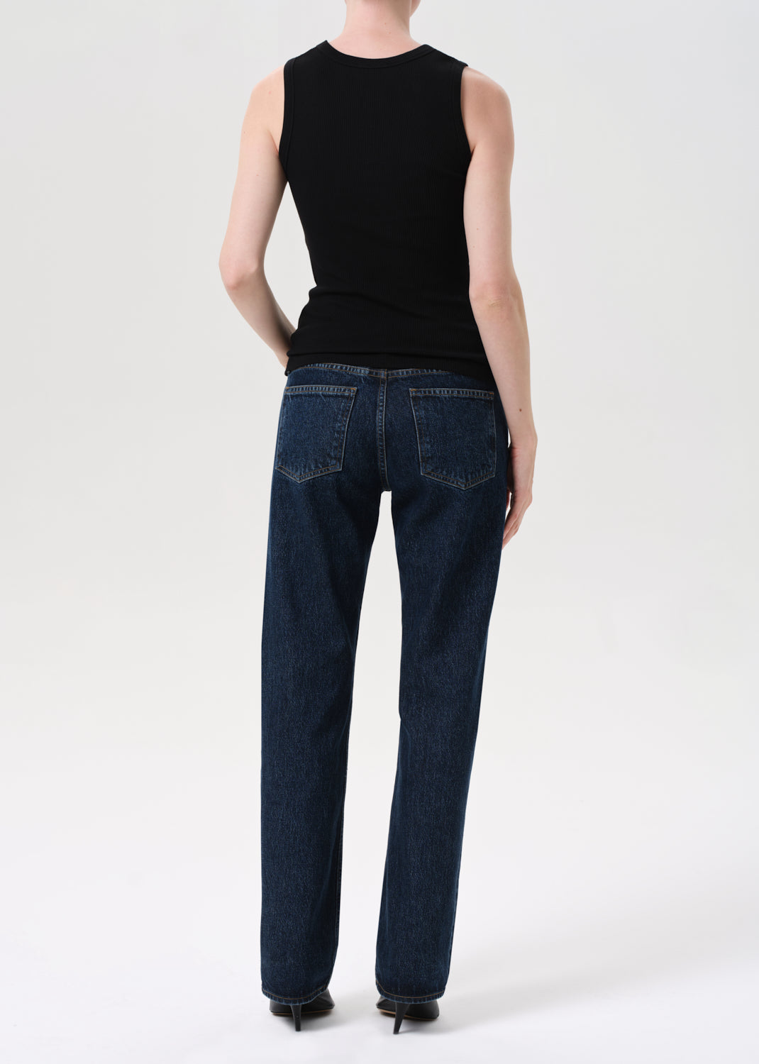 Person wearing a black sleeveless top and blue jeans on a white background