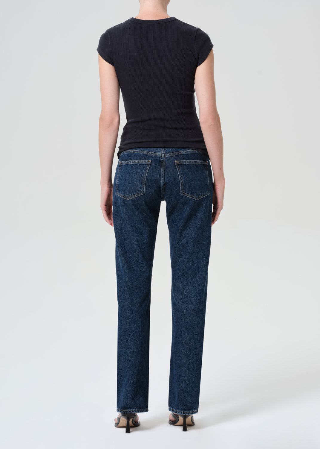 Person wearing blue jeans and a black top on a white background