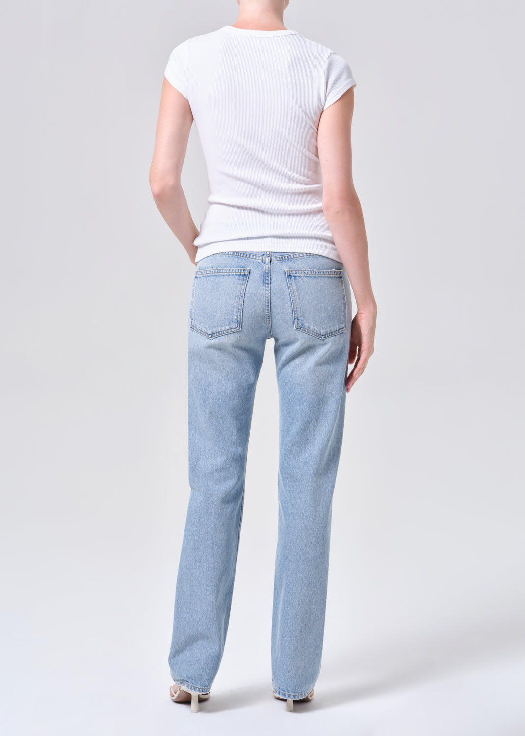 Person wearing light blue jeans and a white t-shirt on a plain background