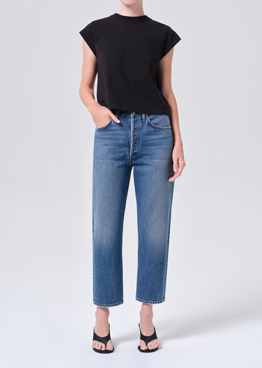 Person wearing blue jeans and a black top on a white background