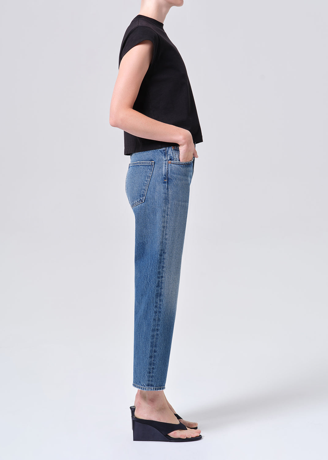 Person wearing a black top and blue jeans on a white background