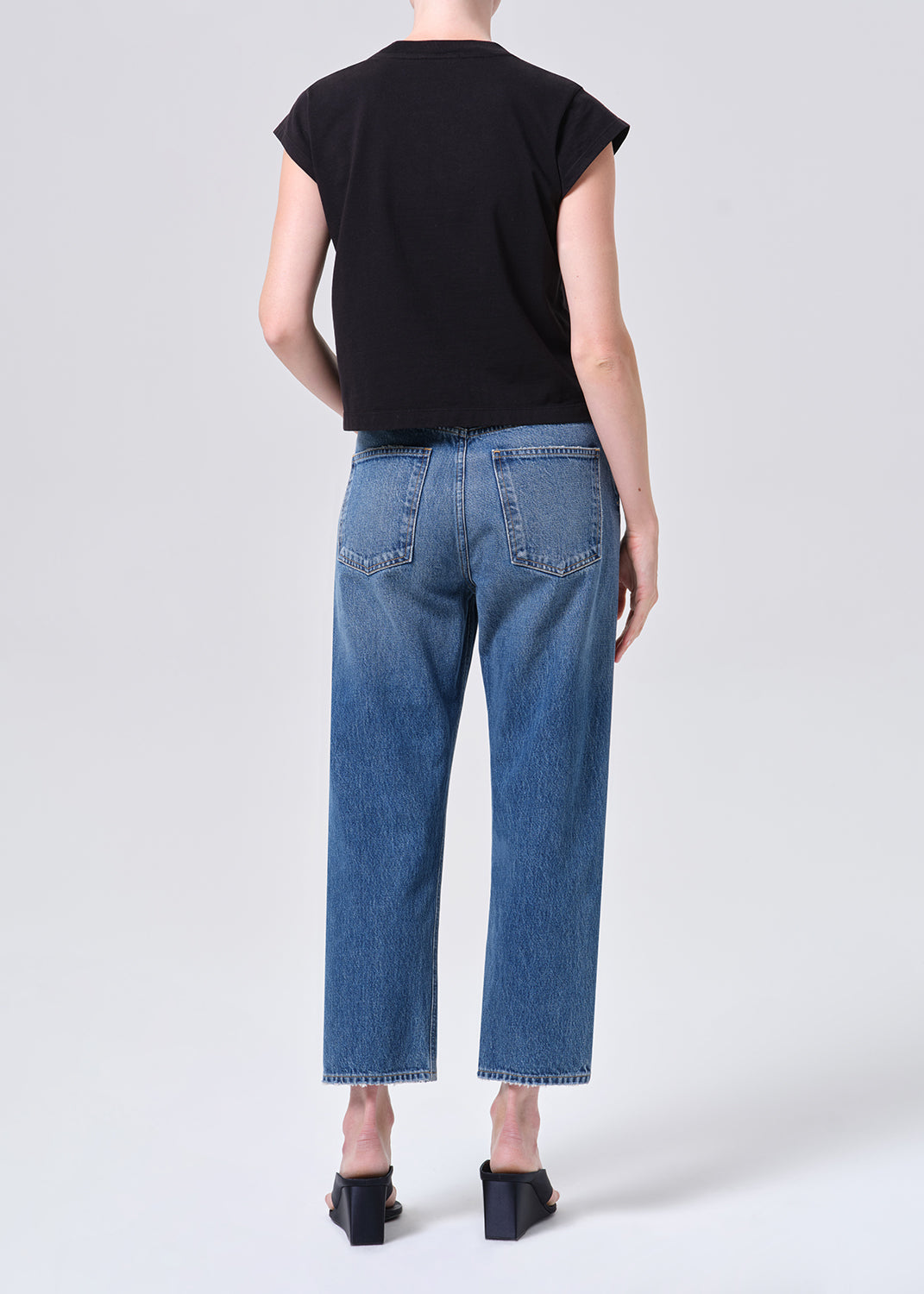 Person wearing blue jeans and a black top on a white background
