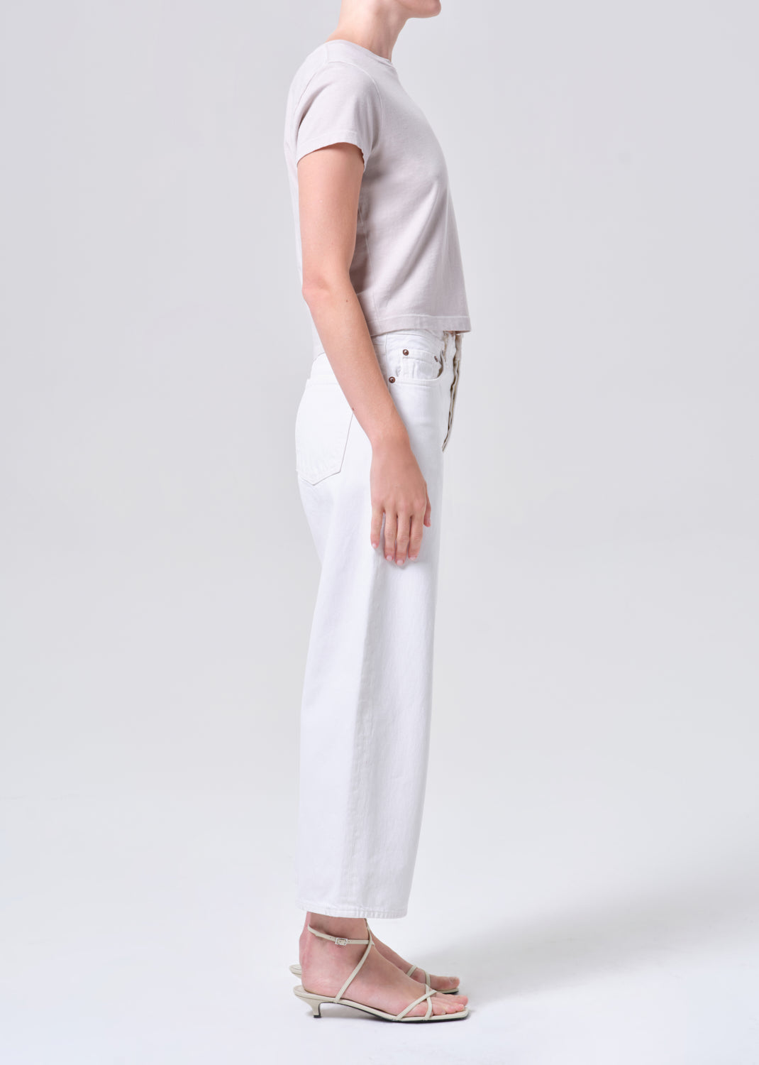 Person wearing a light gray t-shirt and white jeans on a plain background