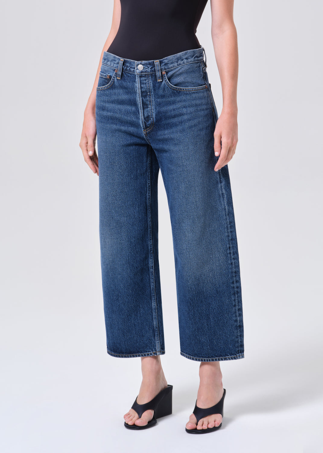 Person wearing blue jeans and black shoes on a white background