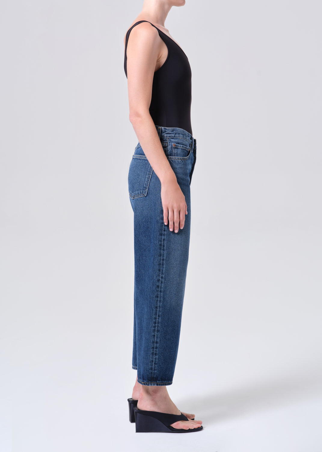 Person wearing blue jeans and a black top on a white background