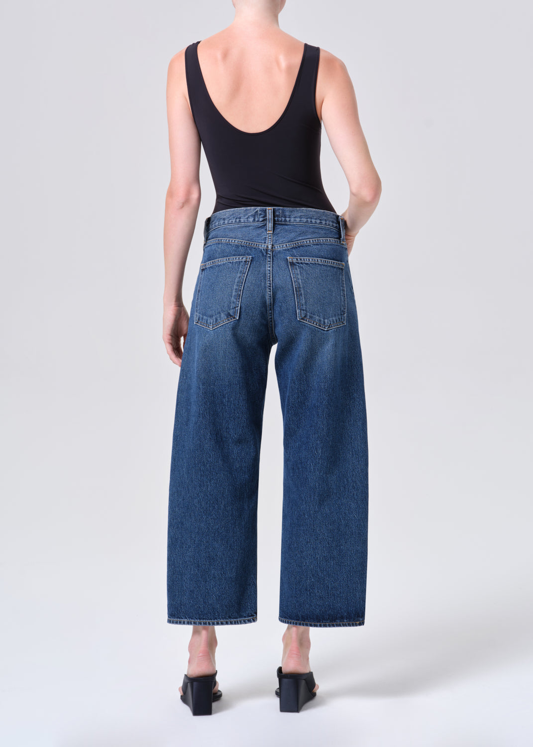 Person wearing blue jeans and a black tank top on a white background