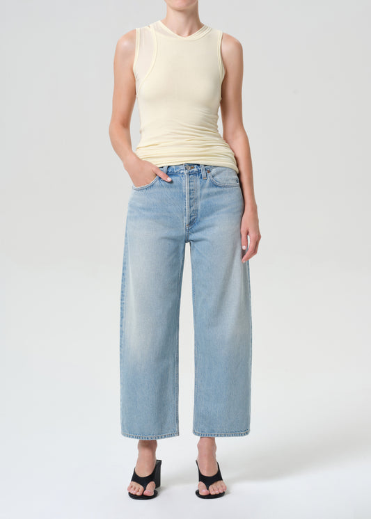 Person wearing a light-colored sleeveless top and wide-leg jeans on a plain background