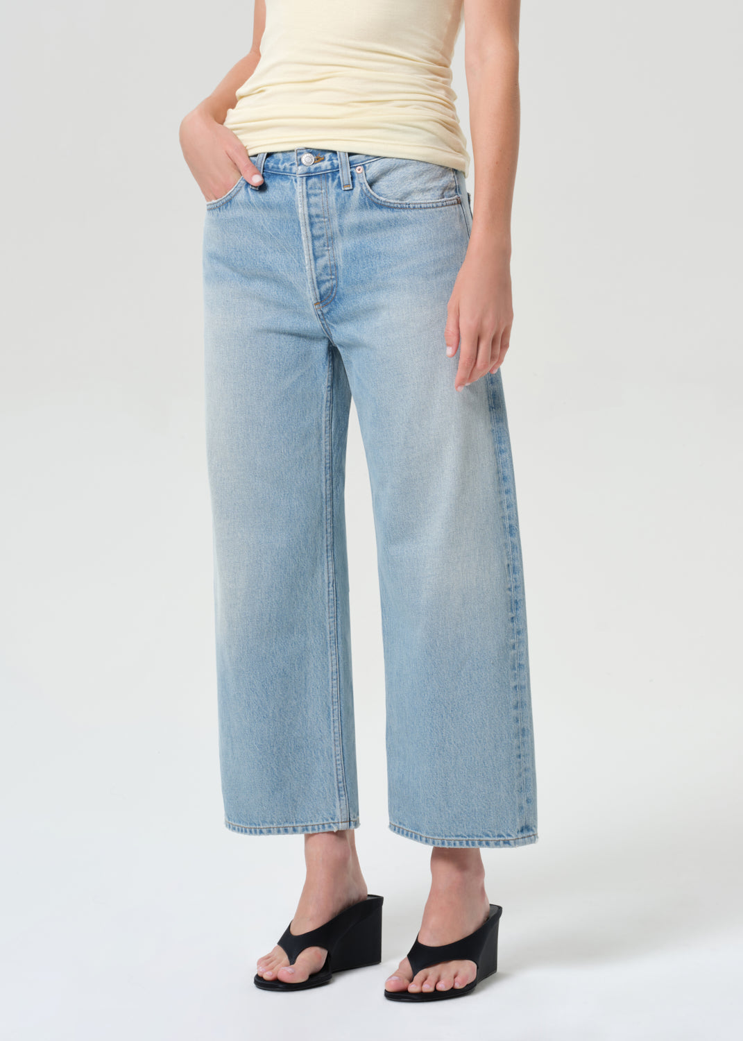 Person wearing light blue jeans and a yellow top on a white background