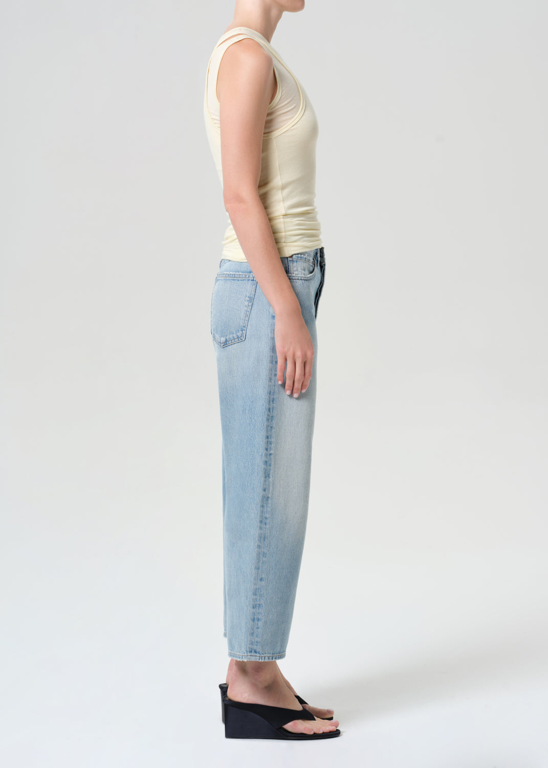 Person wearing a beige tank top and light blue jeans on a white background
