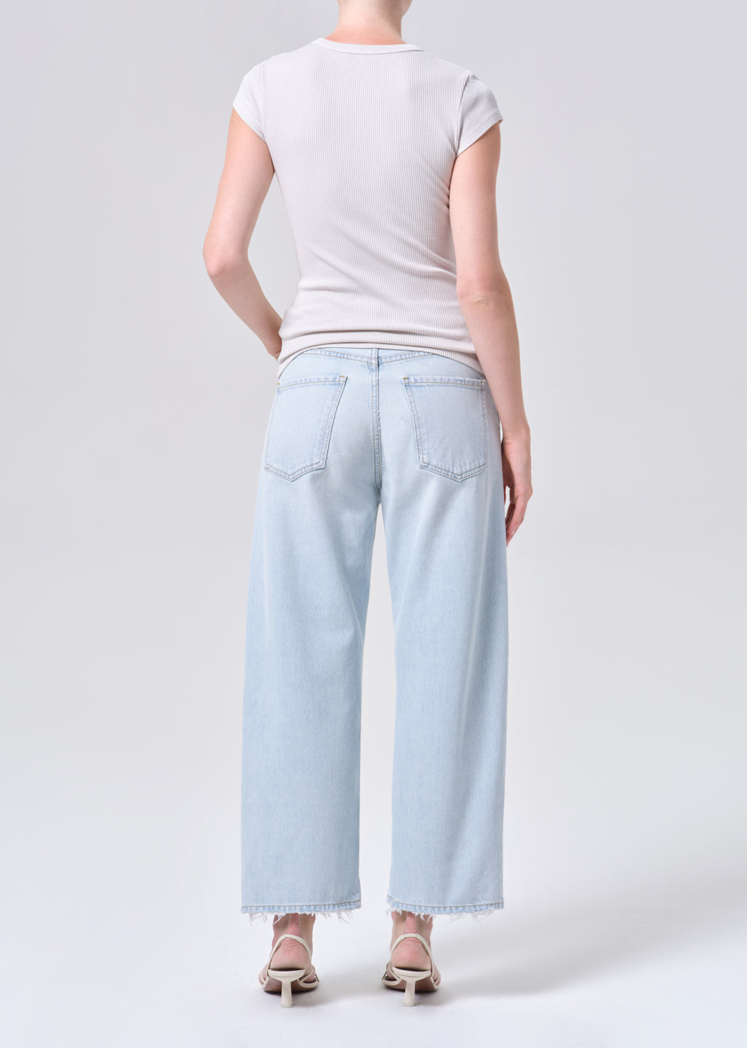 Person wearing light blue jeans and a white t-shirt on a plain background