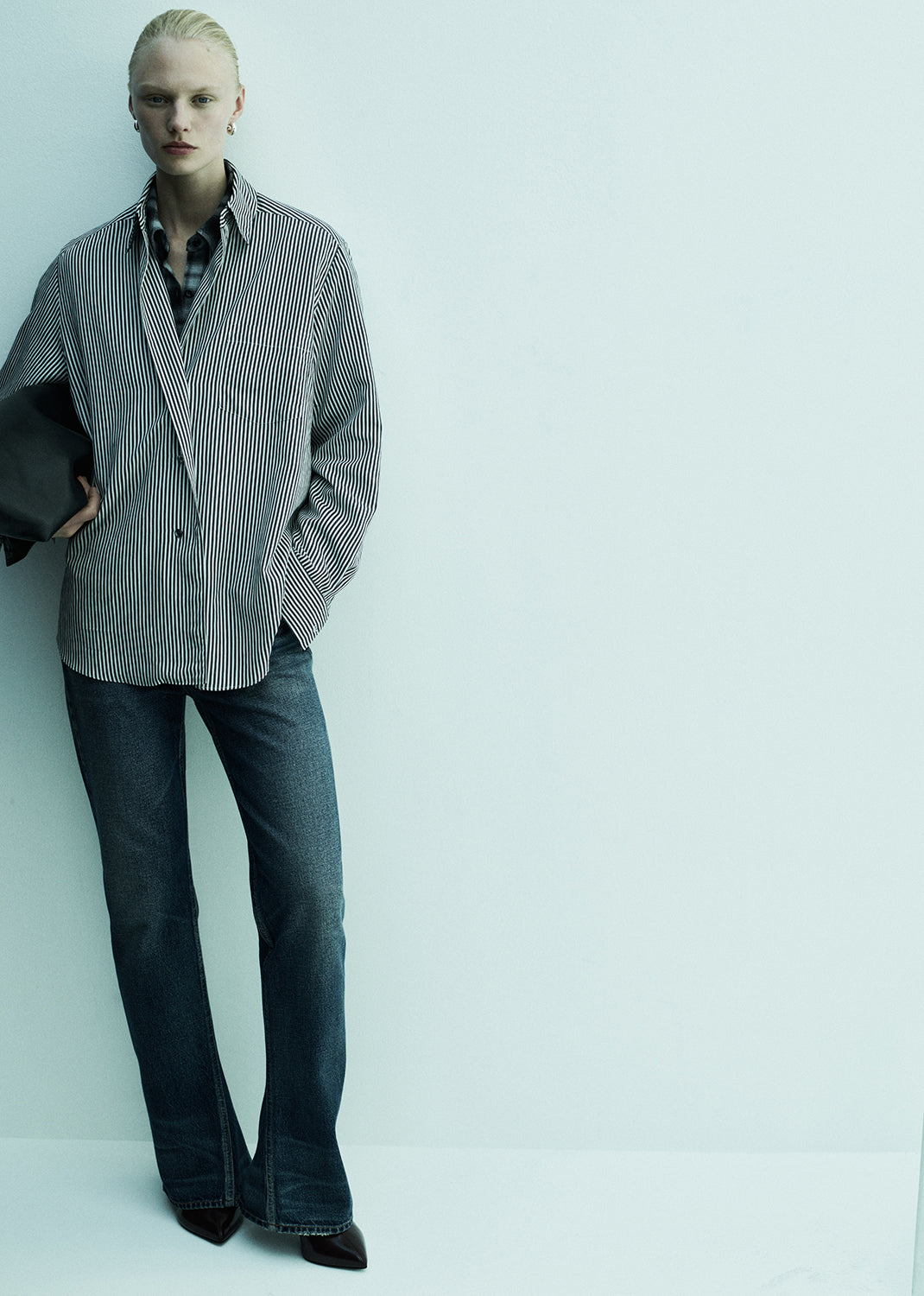 Person wearing a checkered shirt and dark jeans against a light background