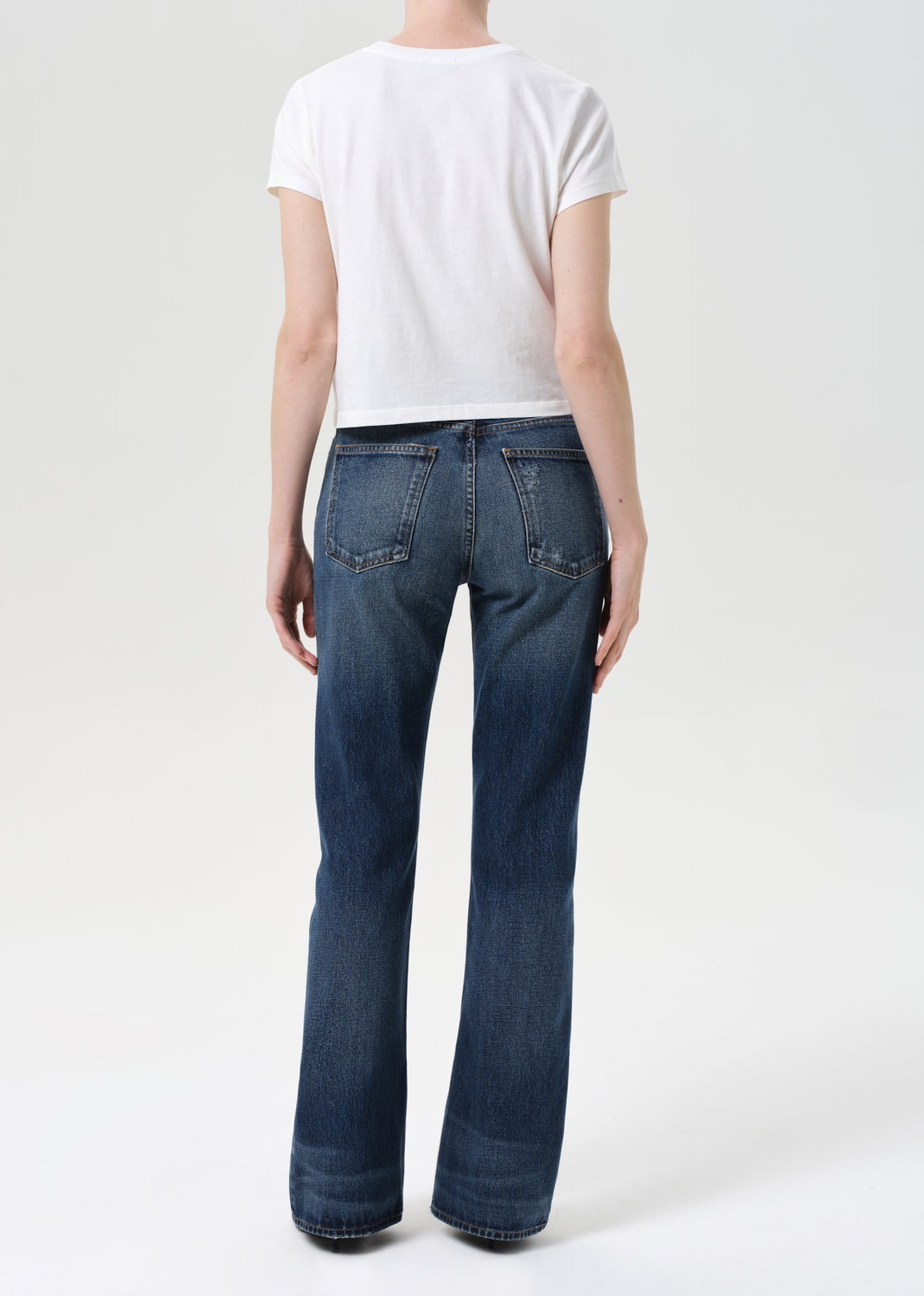 Person wearing blue jeans and a white t-shirt on a plain background