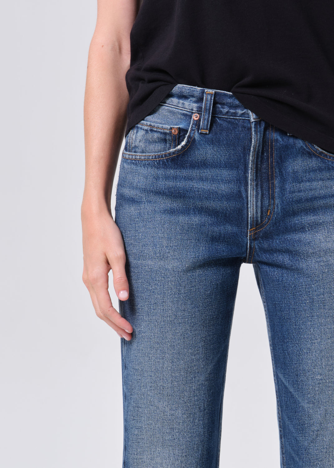 Person wearing blue jeans and a black top on a light gray background