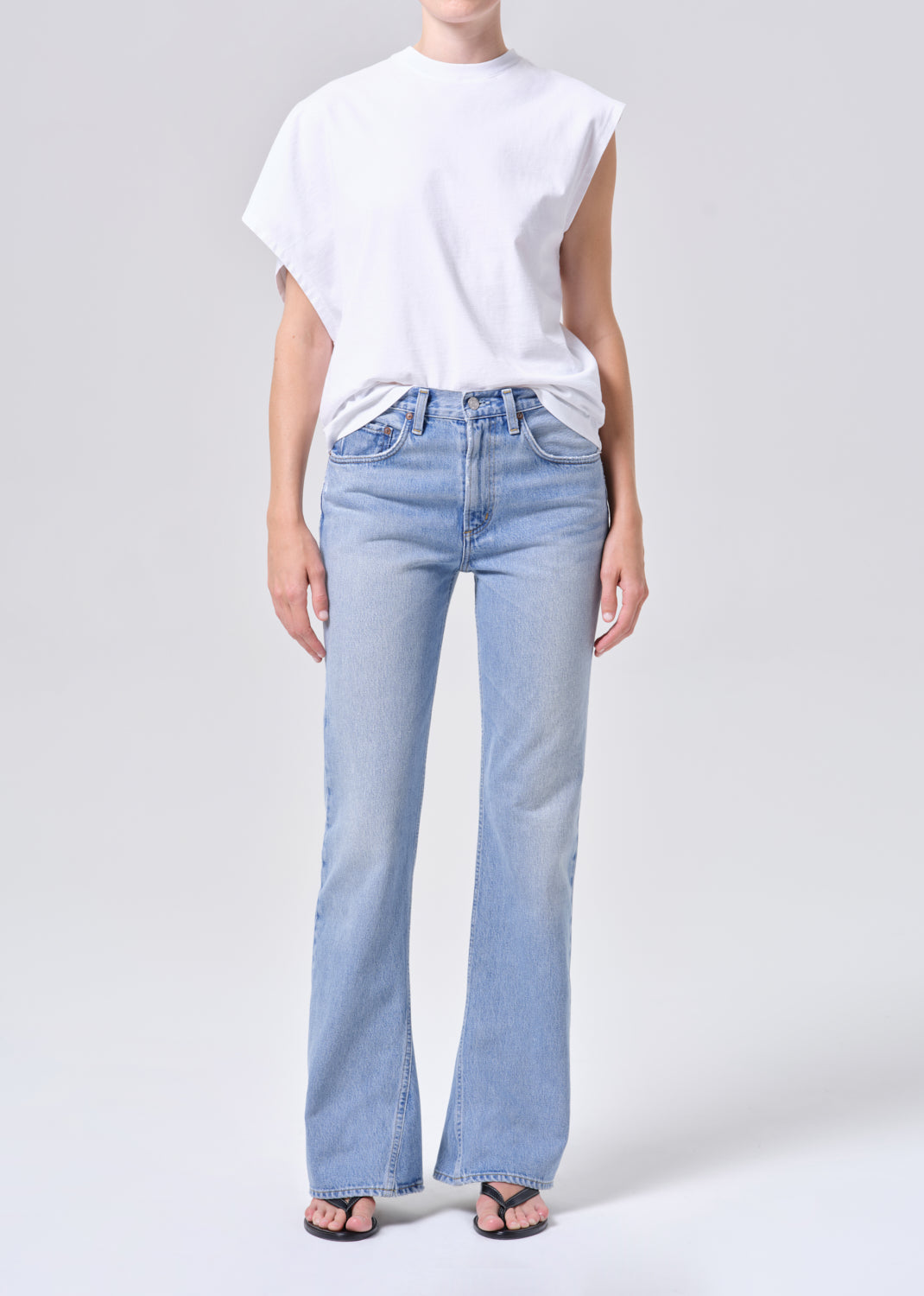 Person wearing light blue jeans and a white t-shirt on a plain background
