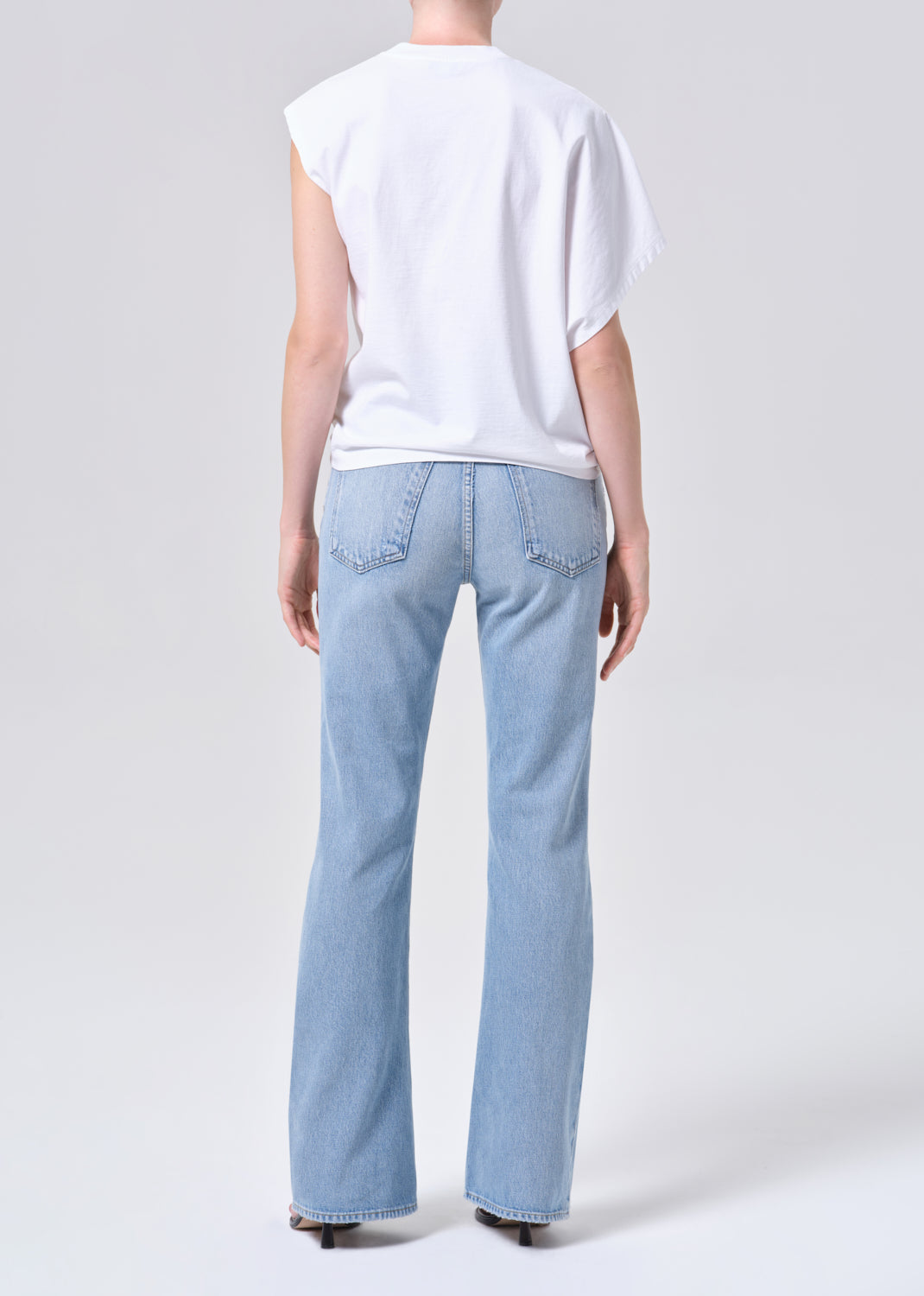Person wearing light blue jeans and a white top on a plain background