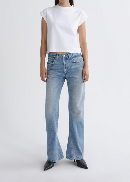 Person wearing a white crop top and light blue jeans on a grey background
