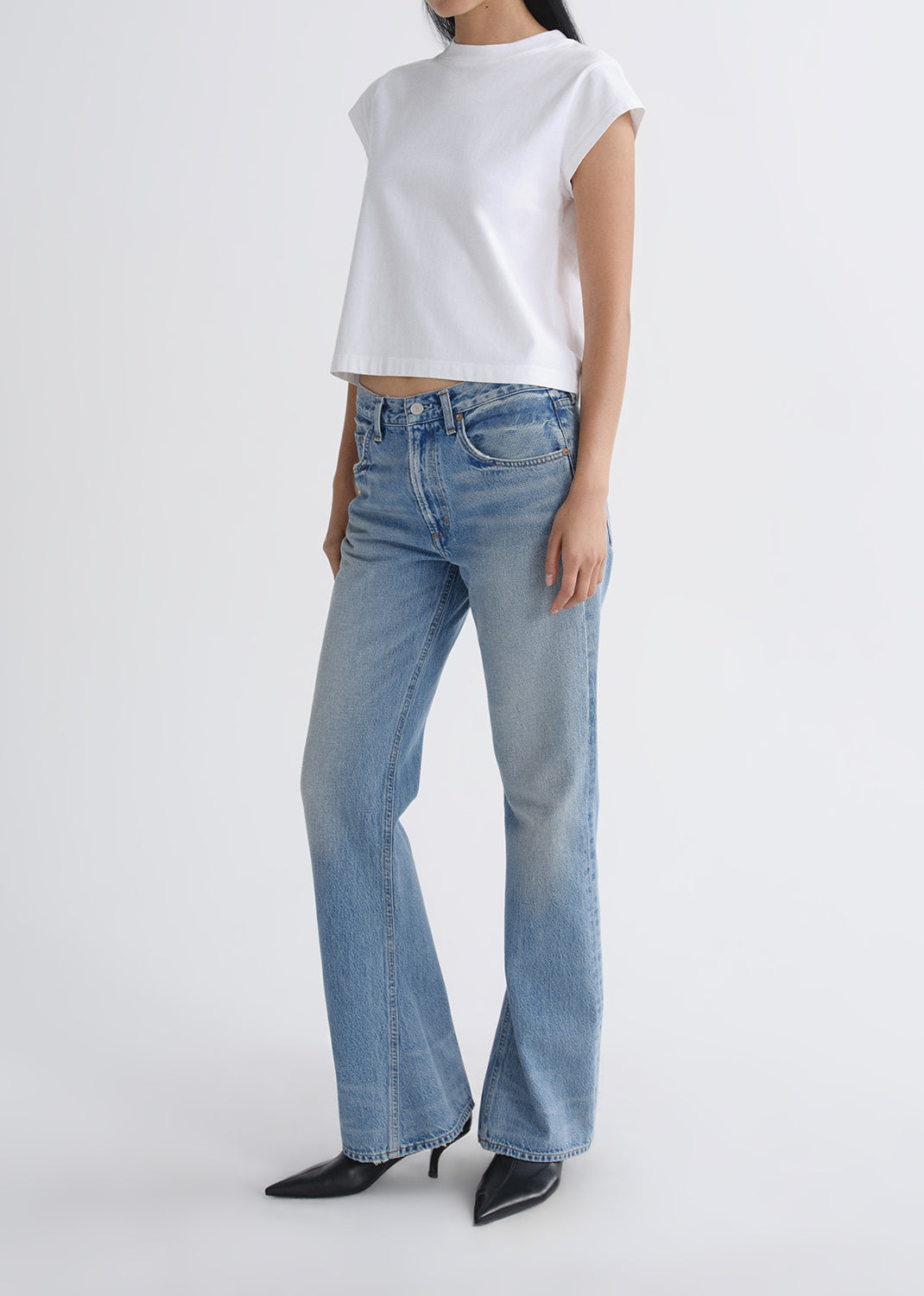 Person wearing a white top and blue jeans on a grey background