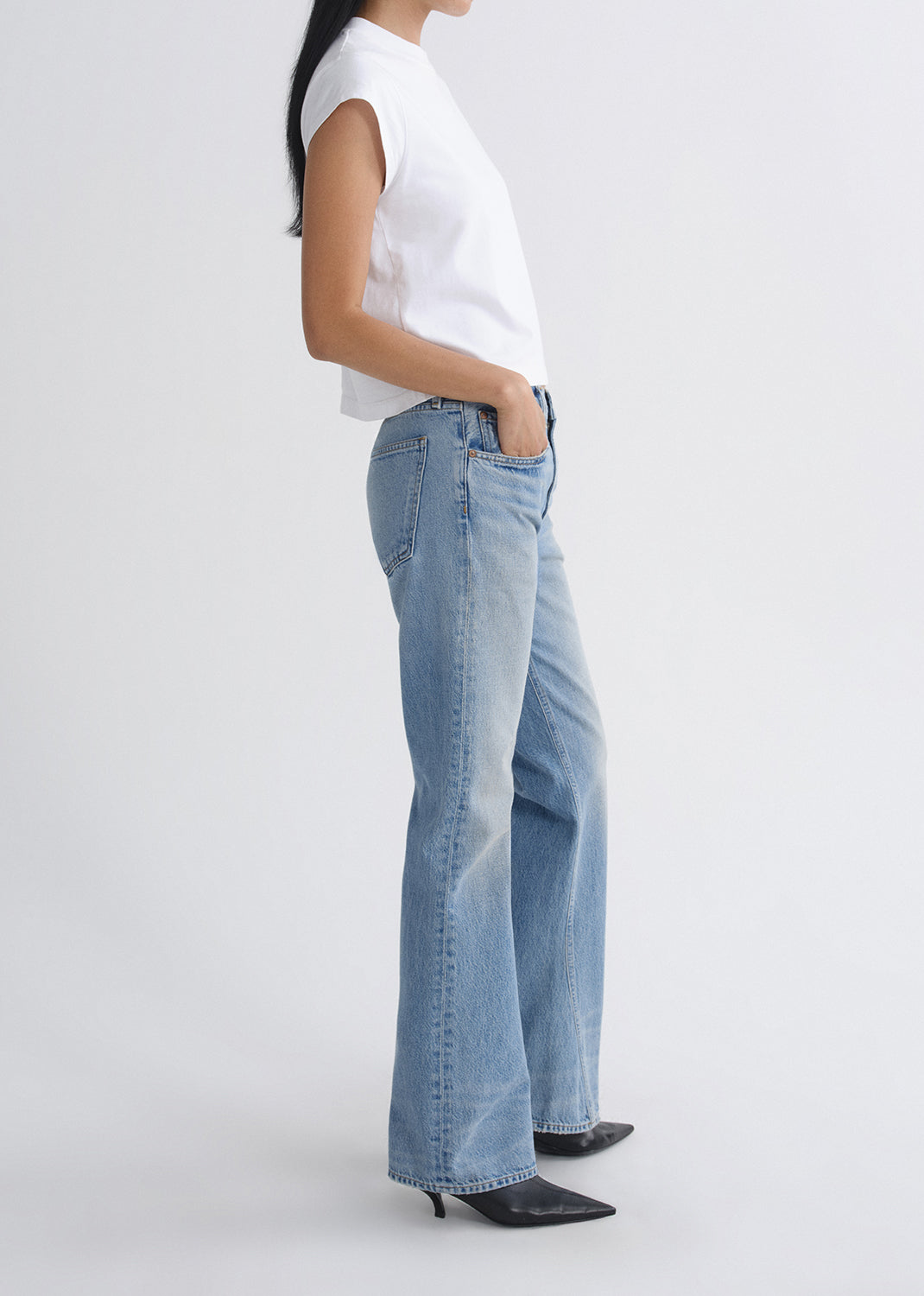 Person wearing light blue jeans and a white top on a grey background