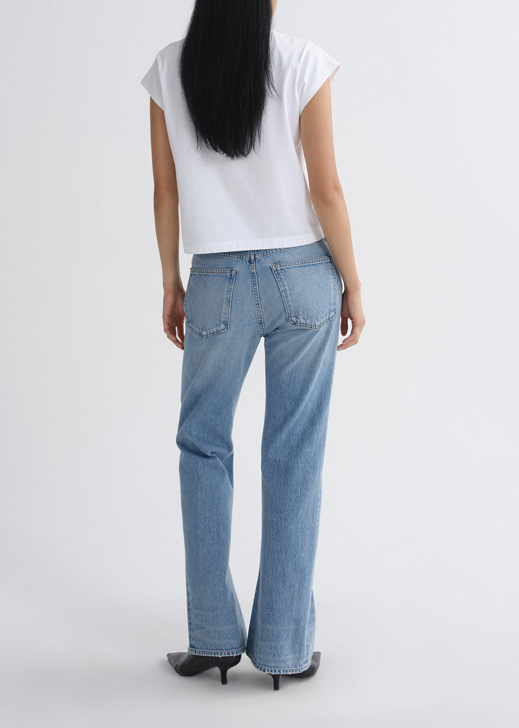 Person wearing light blue jeans and a white top on a grey background