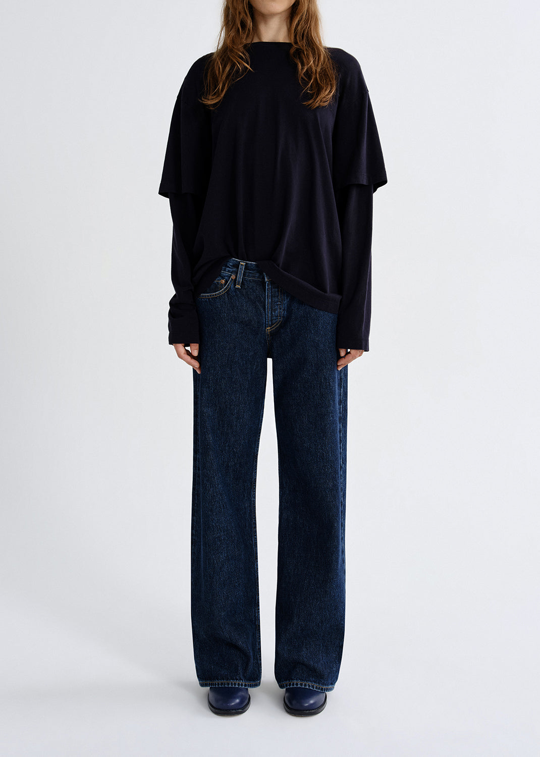 Person wearing black layered top with blue pants on a grey background