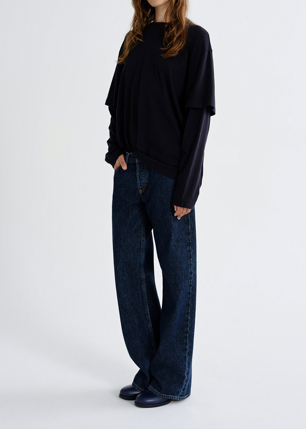 Person wearing black layered top with blue pants on a grey background