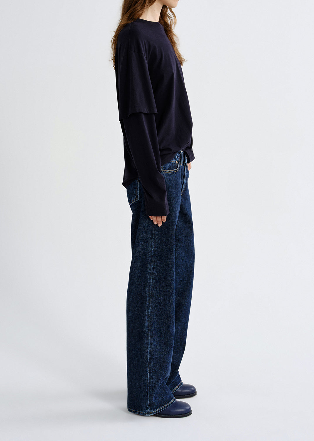 Person wearing black layered top with blue pants on a grey background