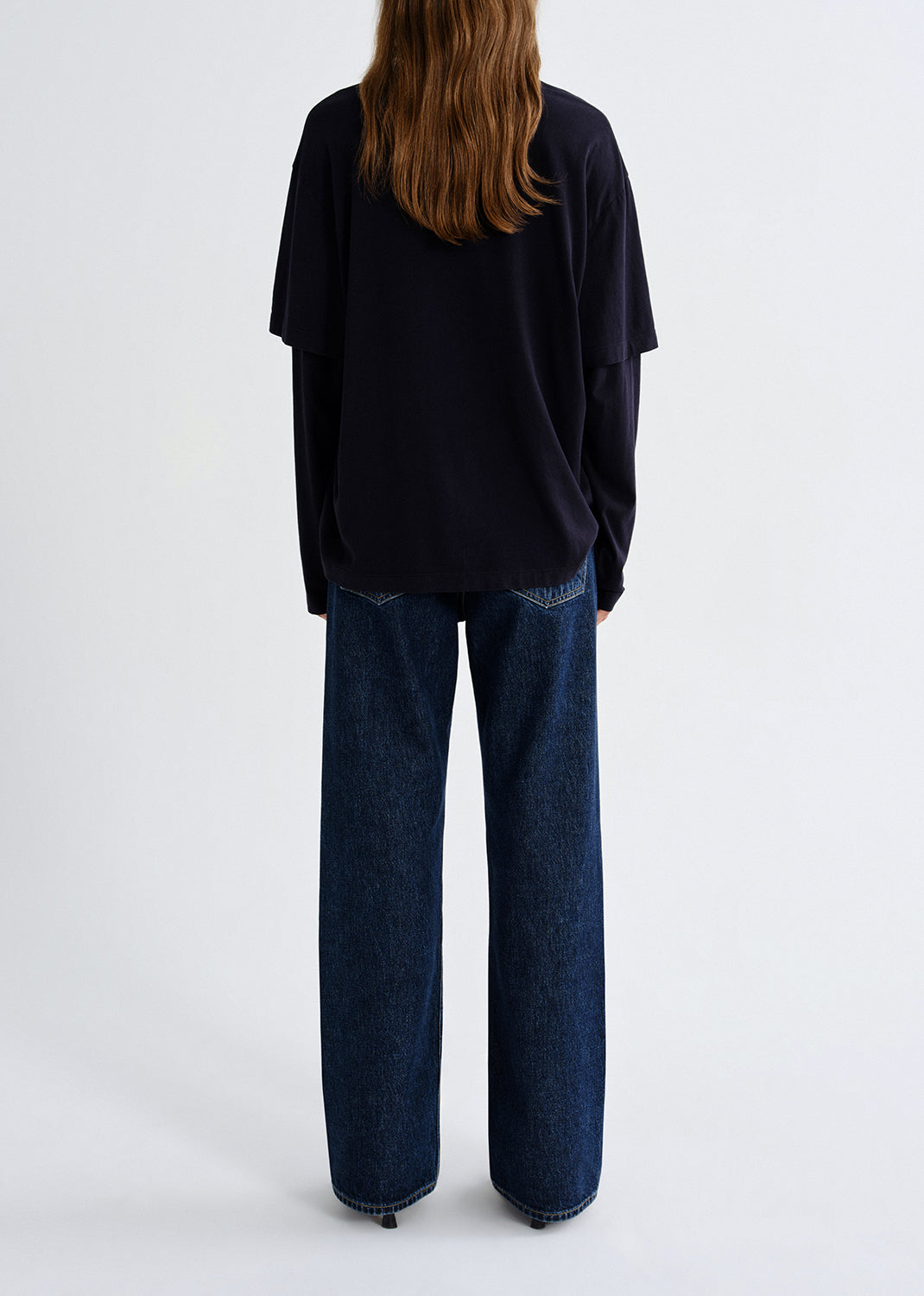 Person wearing black layered top with blue pants on a grey background