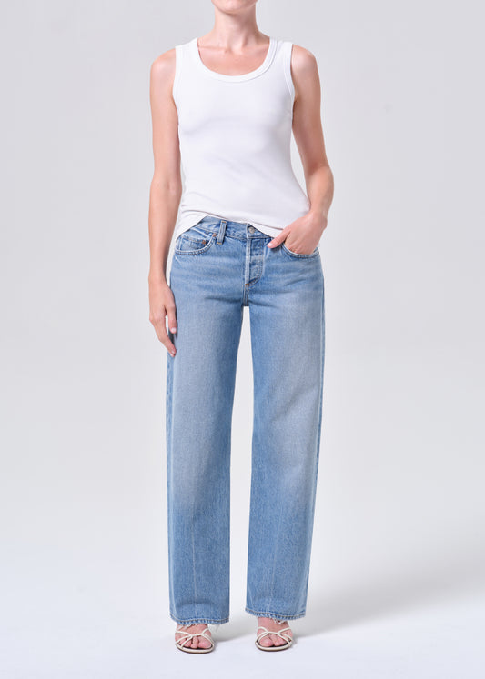 Person wearing light blue jeans and a white tank top on a white background