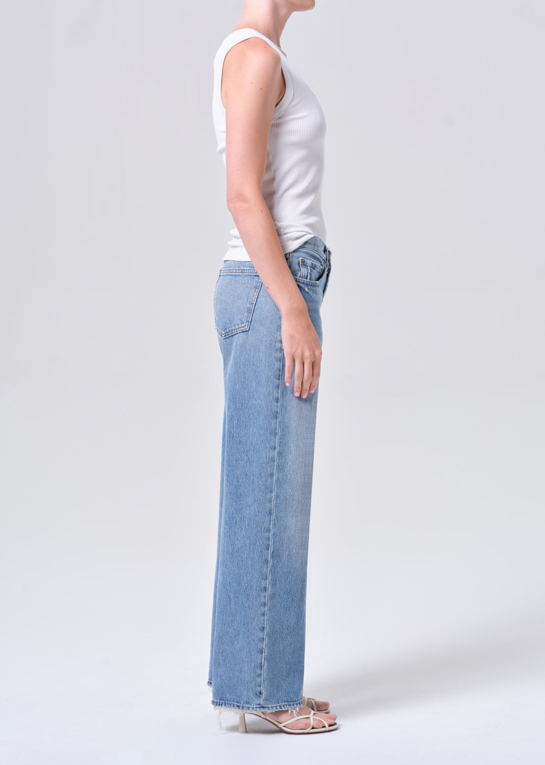Person wearing light blue jeans and a white top on a plain background