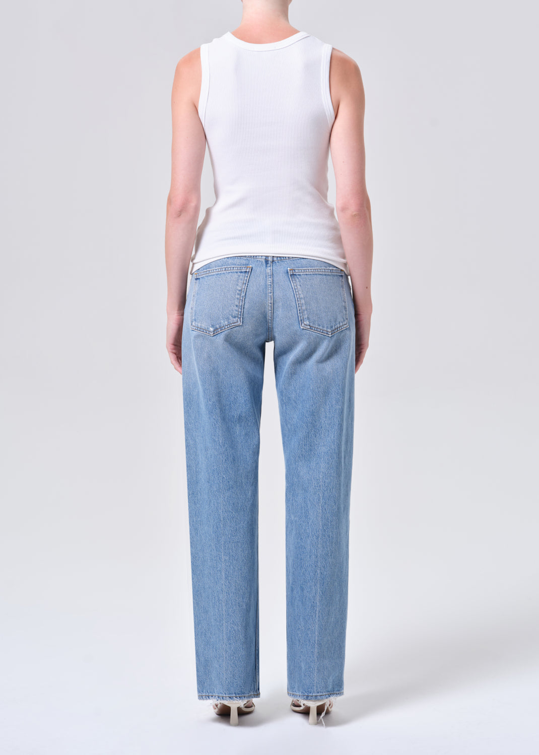 Person wearing light blue jeans and a white sleeveless top on a white background