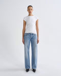 A model stands against a light gray studio background wearing a white short-sleeve crewneck t-shirt and light-wash blue straight-leg jeans with black pointed shoes.