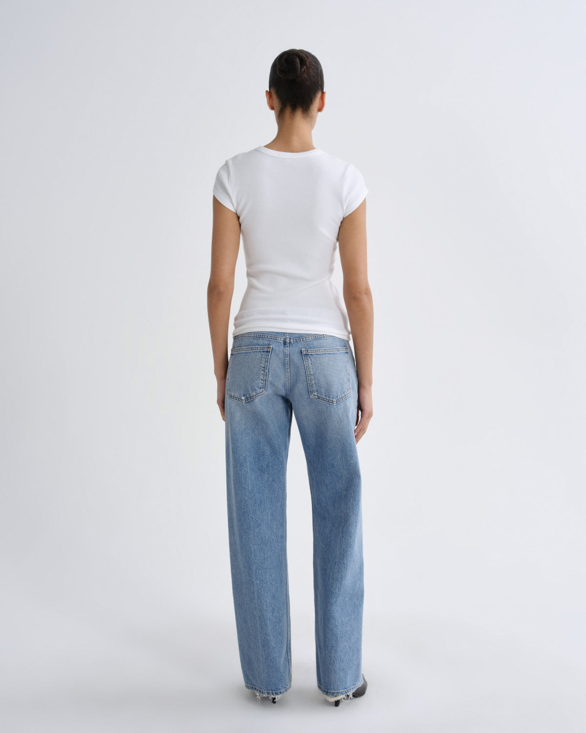 A model shown from the back wearing a white short-sleeve t-shirt and light blue wide-leg jeans against a plain light gray studio background.