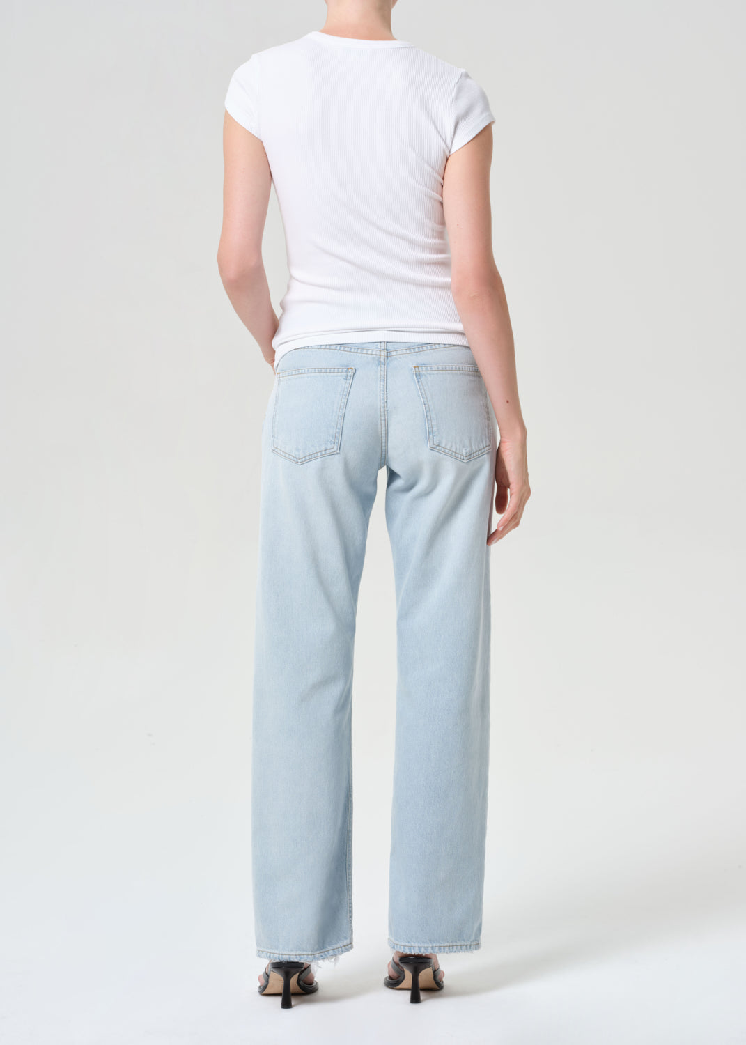 Person wearing light blue jeans and a white t-shirt on a plain background