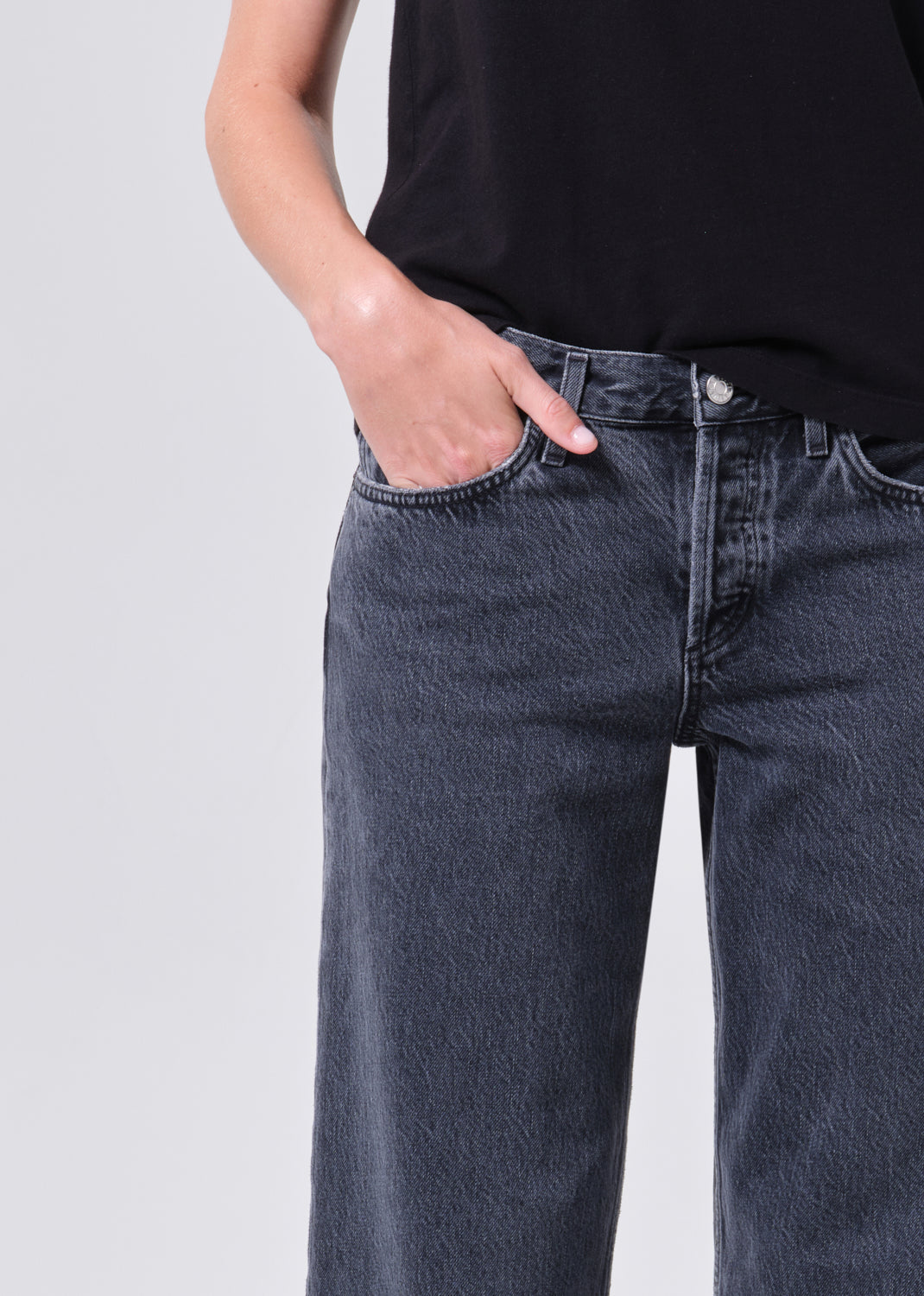 Person wearing dark blue jeans and a black shirt on a light gray background