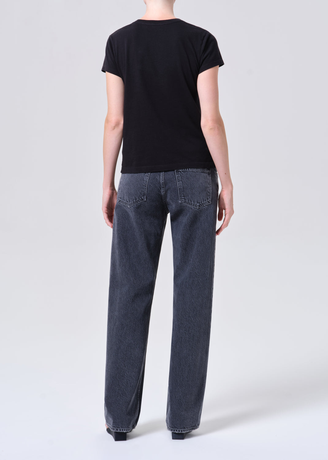 Person wearing a black t-shirt and blue jeans on a white background