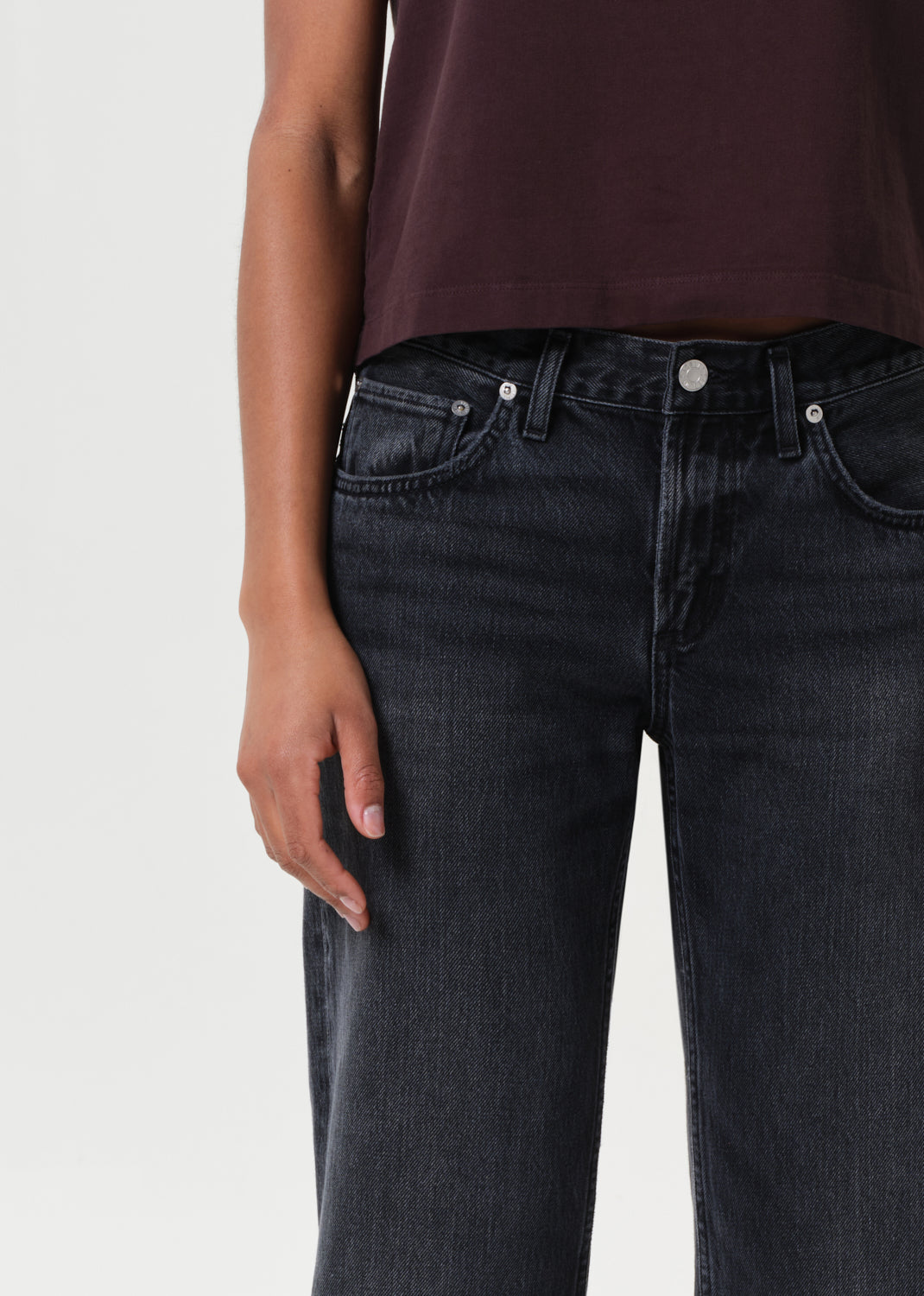 Person wearing dark jeans and a maroon top on a light gray background