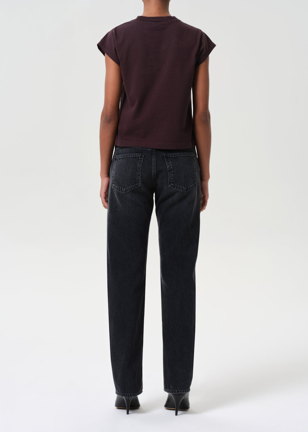 Person wearing a dark brown t-shirt and black jeans on a white background