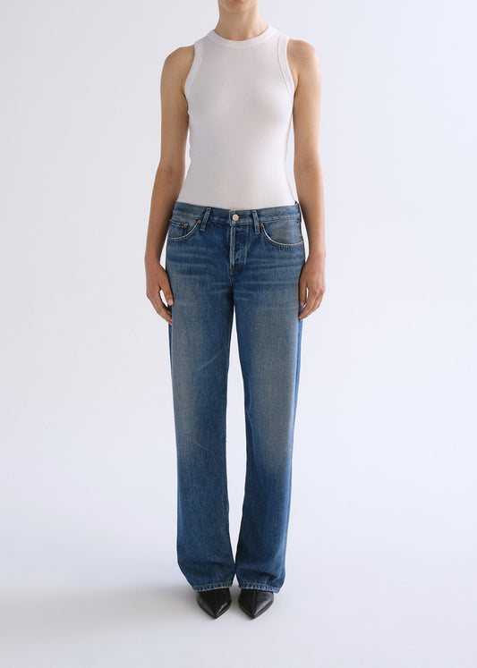 Person wearing white tank top with blue jeans on a grey background