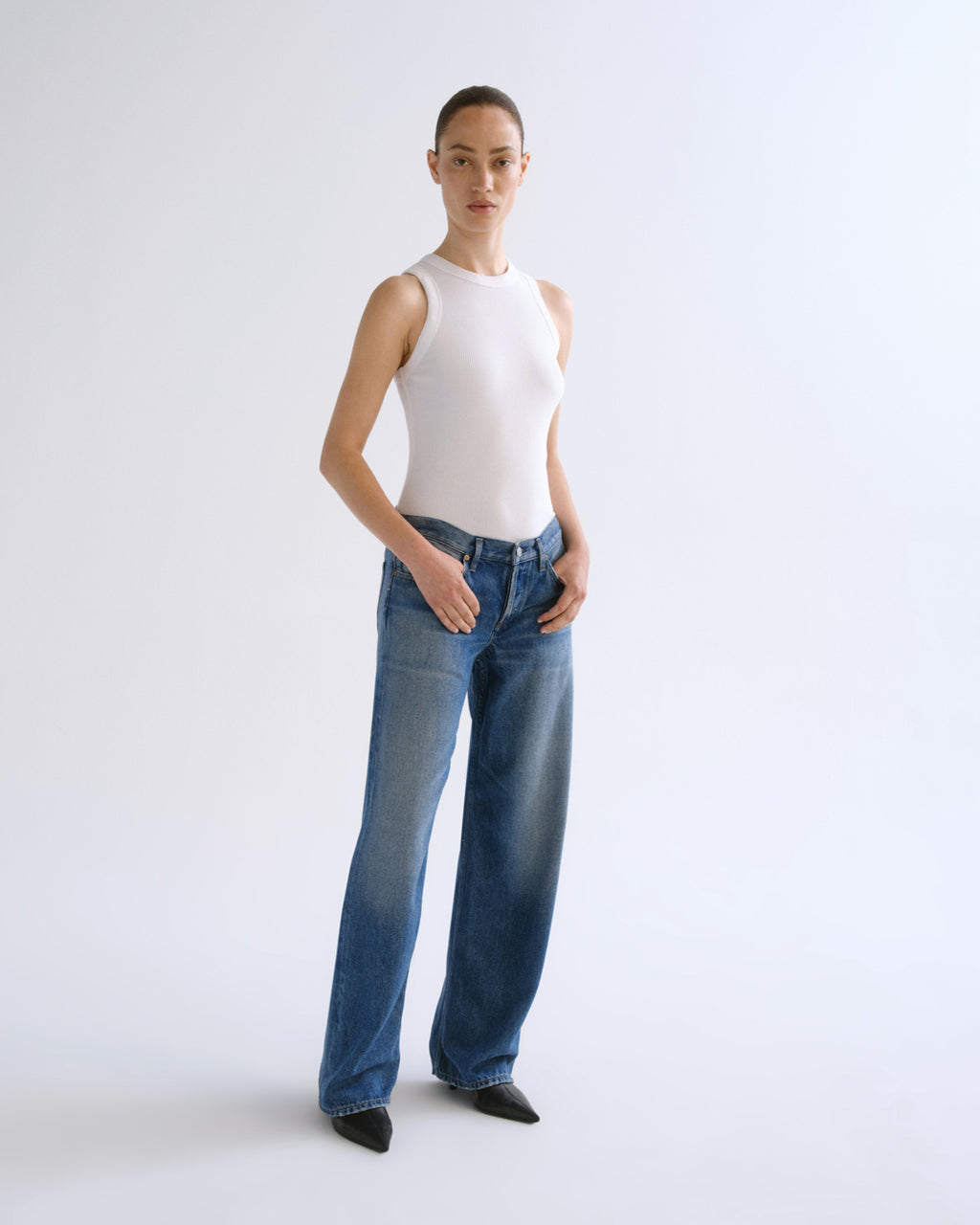 A model shown from the back wearing a white ribbed tank top and wide-leg blue denim jeans against a plain white studio background.