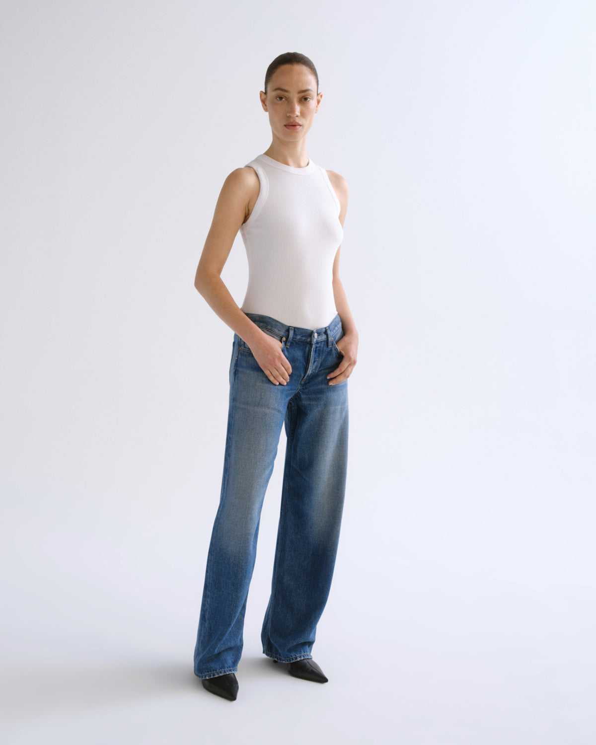 A model shown from the back wearing a white ribbed tank top and wide-leg blue denim jeans against a plain white studio background.