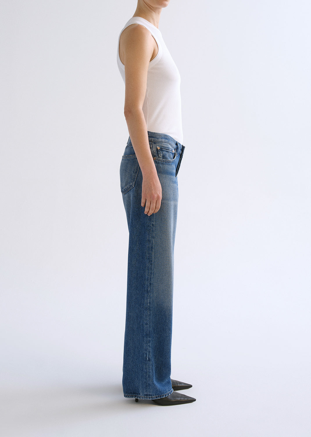 Person wearing white tank top with blue jeans on a grey background