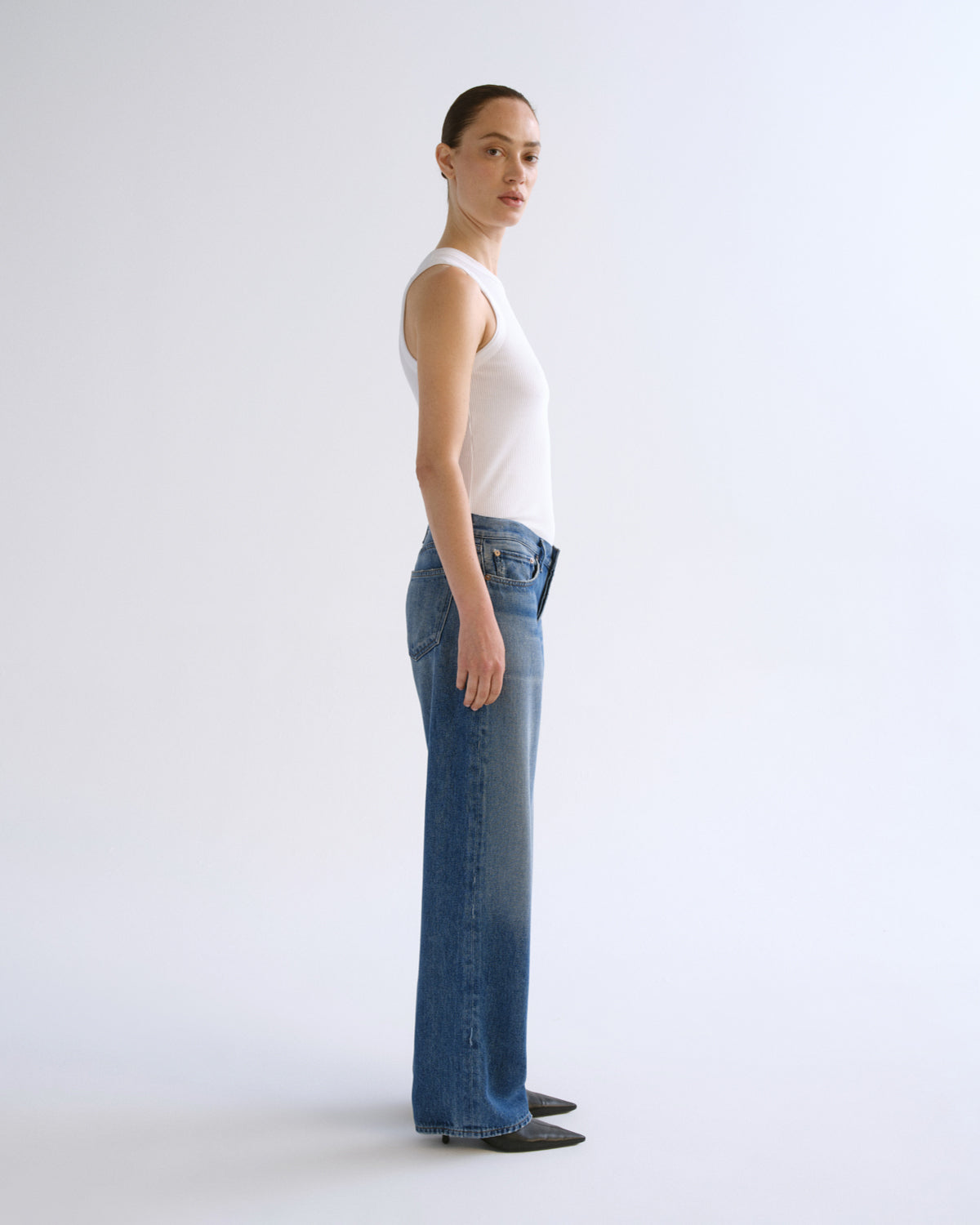A model shown from the back wearing a white ribbed tank top and wide-leg blue denim jeans against a plain white studio background.