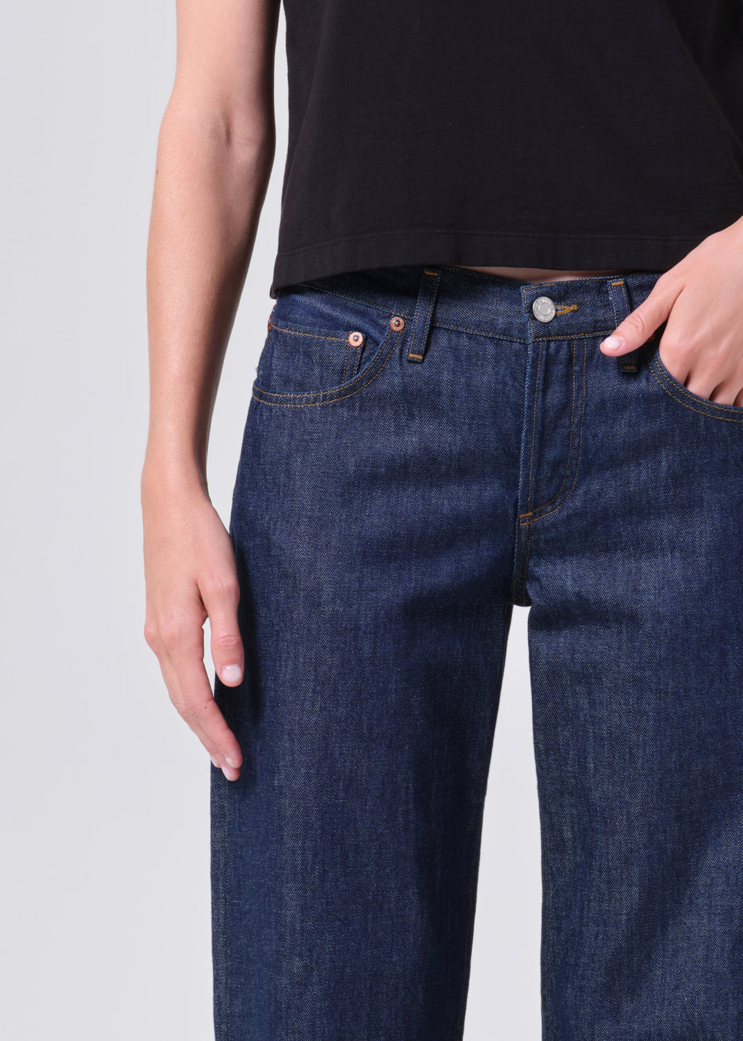Person wearing dark blue jeans and a black top on a light gray background