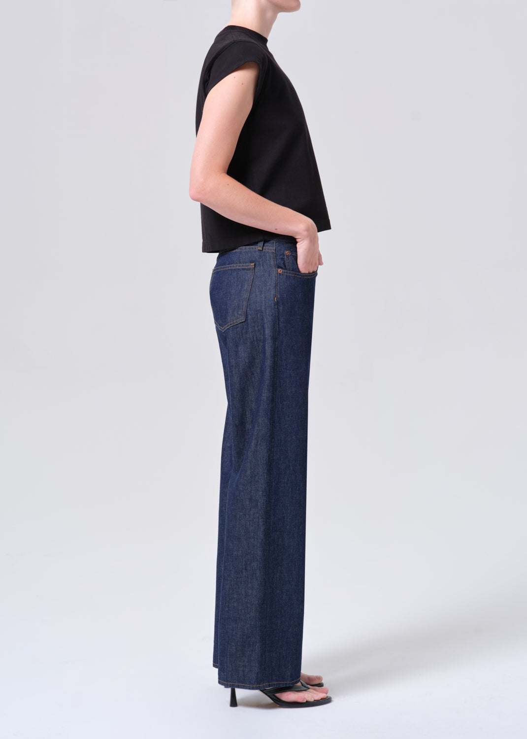 Person wearing a black sleeveless top and blue jeans on a white background